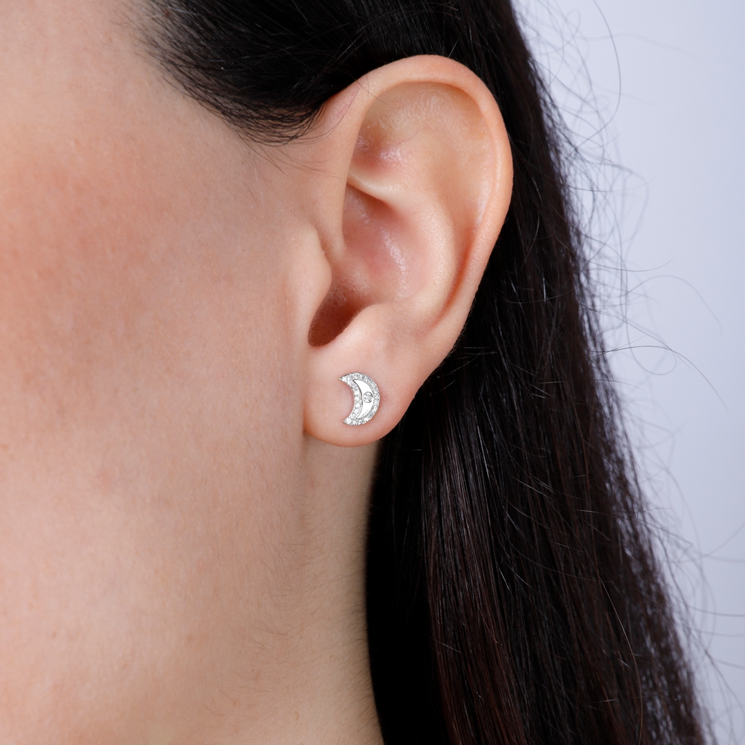 A woman with long brunette hair is wearing a pair of stud earrings with a half-moon design with sparkling diamonds that are set on the back. 