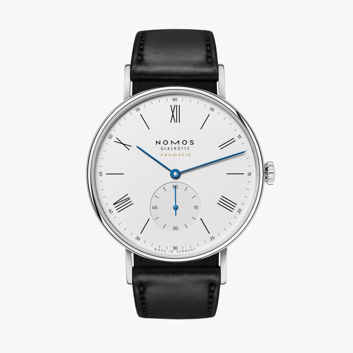 A Nomos Glashutte watch stands straight against a white background. It features a white dial, blue hands and markers, a stainless steel bezel, and a black strap.