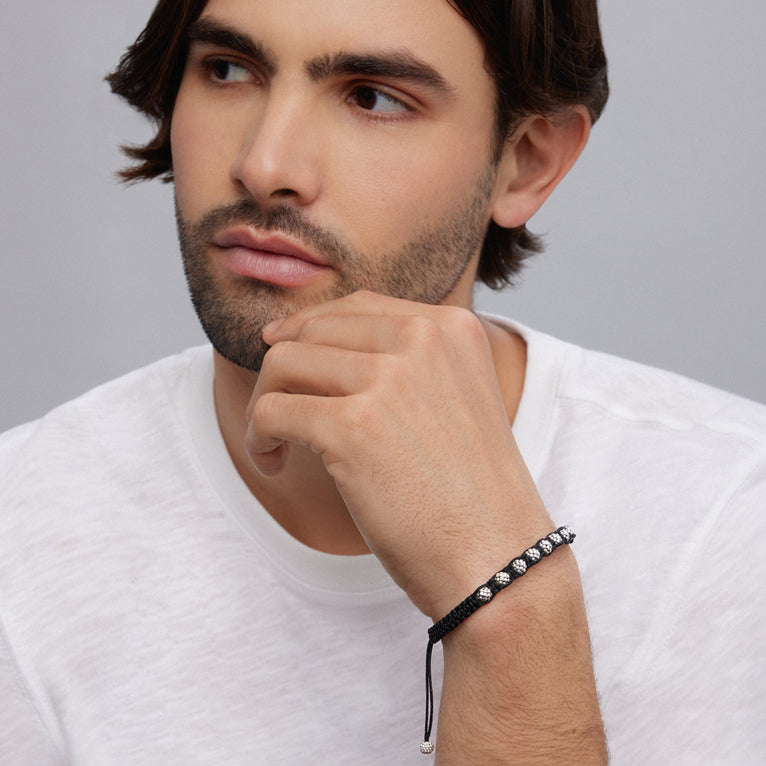 A man is wearing a black bracelet featuring braided nylon with sterling silver Caviar beads.