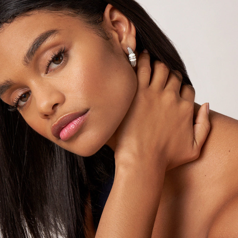 A woman wearing a pair of hoop earrings with white ceramic and a diamond station with sterling silver Caviar beads. 