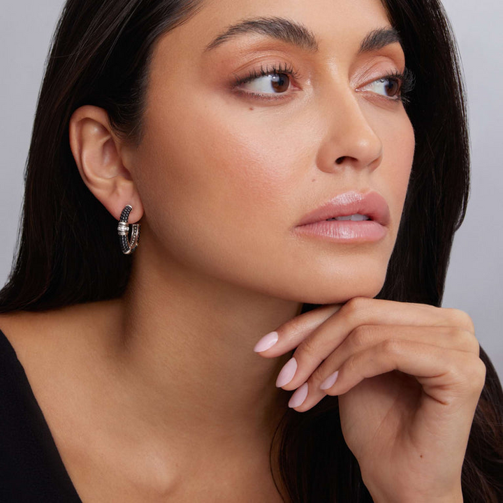 A woman wearing a black top and a pair of hoop earrings with Black ceramic Caviar beading, sterling silver, and diamonds.