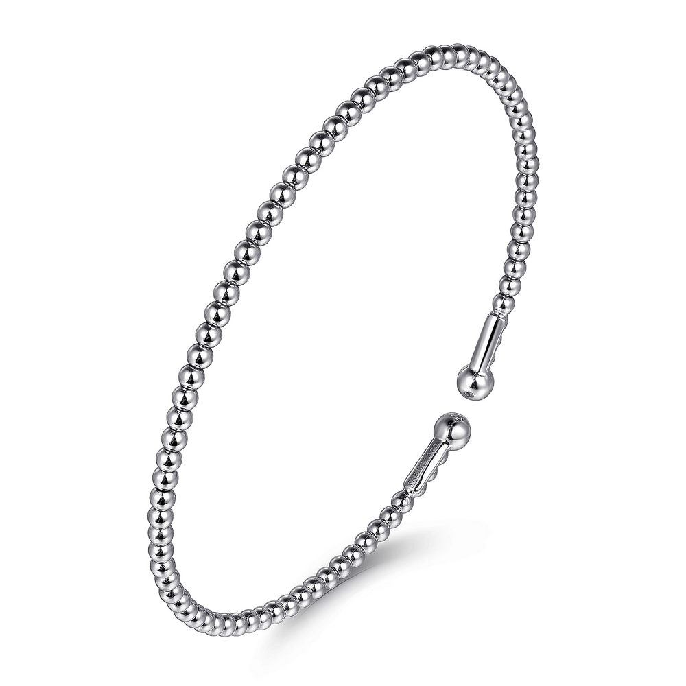 A white-gold bangle bracelet with a beaded band and end caps is angled in the middle of a white background.