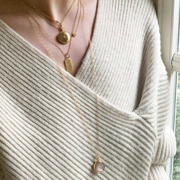 A woman is wearing a Petite Mother of Pearl Locket and a white sweater.