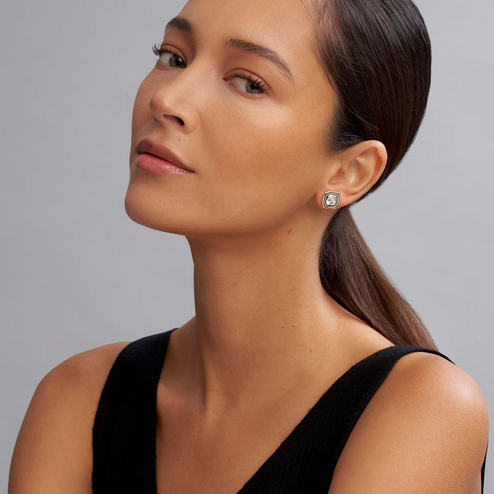 A woman is wearing a black tank top and a pair of stud earrings with a White topaz gemstone surrounded by sterling silver and 18k gold Caviar beading. 