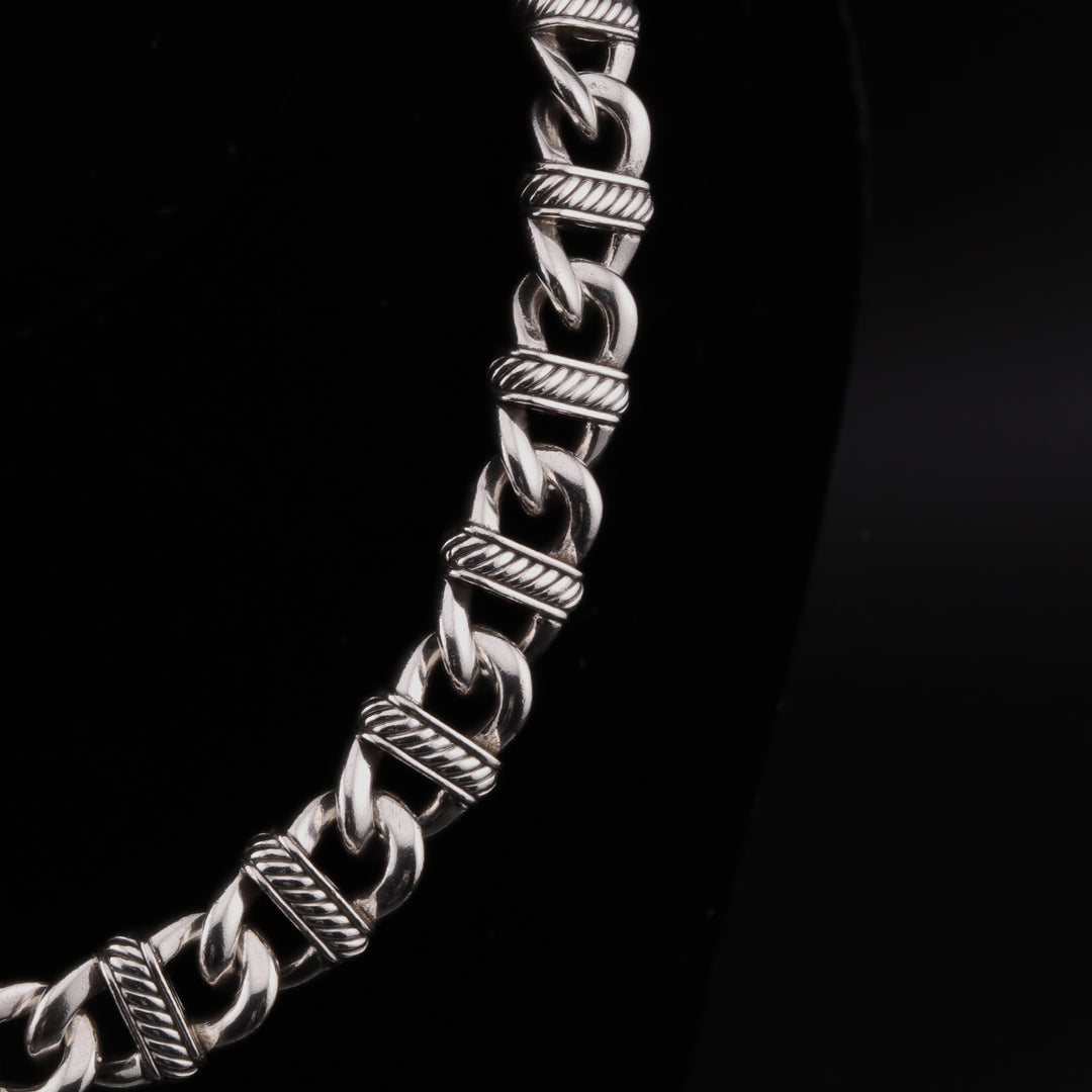 A close-up showing the right side of a sterling silver chain necklace with curb links and detailed stations against a black background.