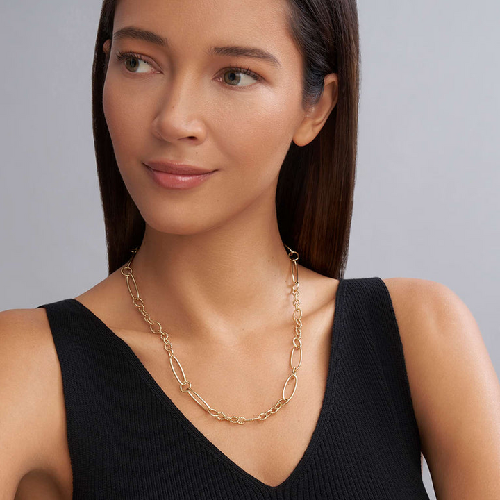 A close-up of a woman wearing an 18k gold link necklace featuring caviar beading and fluting elements.