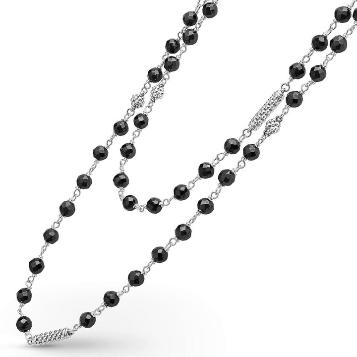 A sterling silver and ceramic beaded necklace angled to the right in the middle of a white background featuring black ceramic and silver Caviar beading.