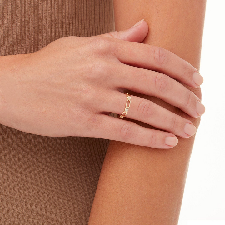 A close-up of a woman wearing a yellow-gold ring. The ring features alternating links and diamond-set bezel pattern stacks.