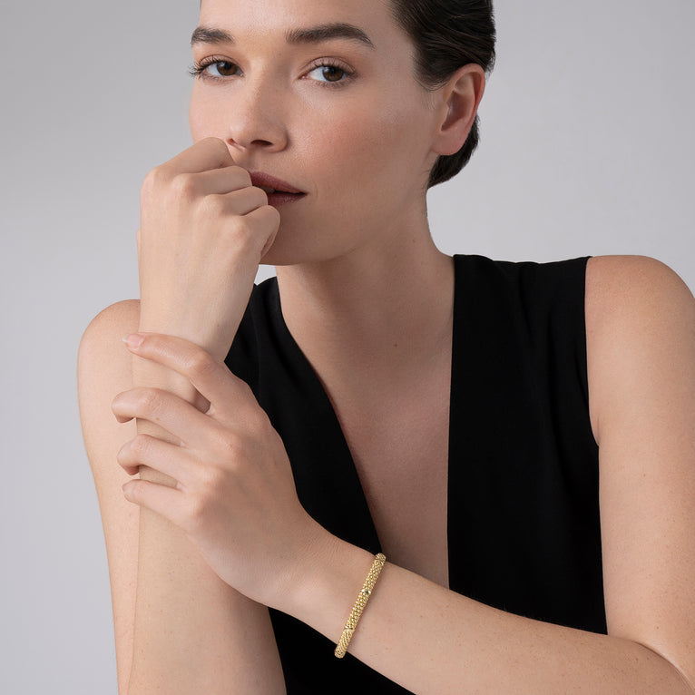 A close-up of a woman wearing a black blouse and an 18k gold bracelet. The bracelet features smooth stations and caviar beading.