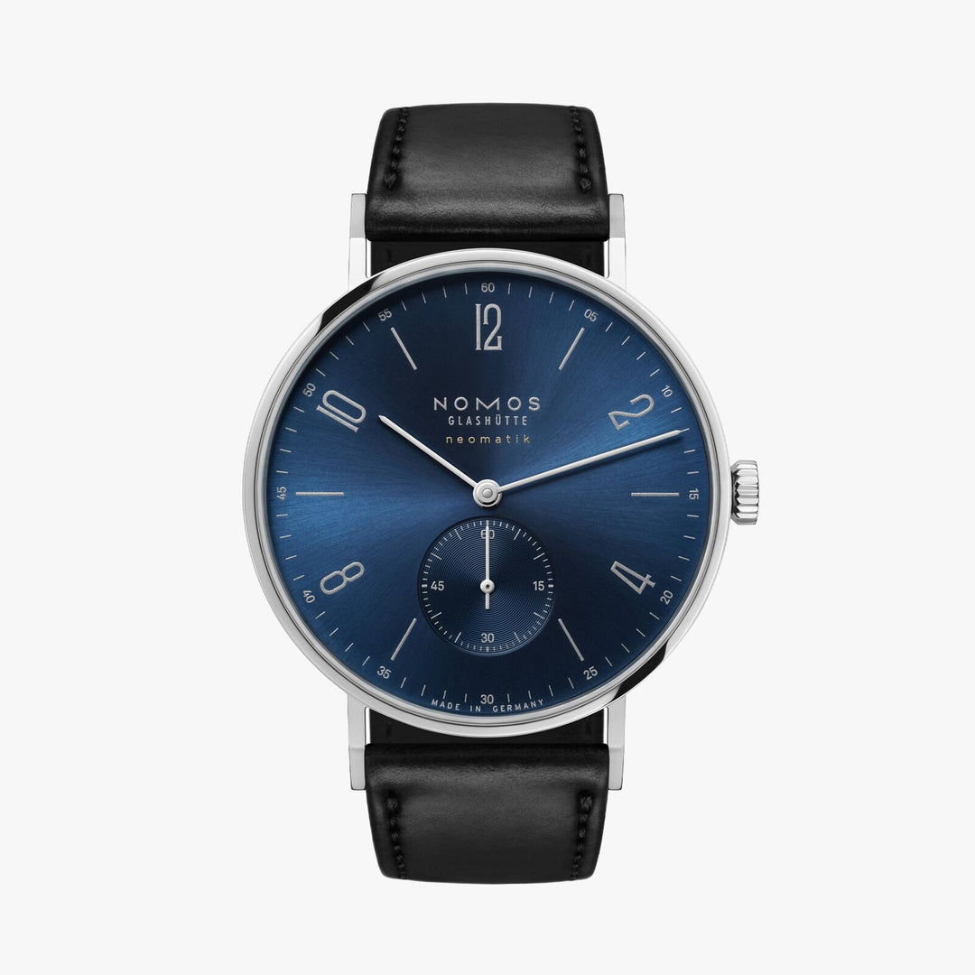 A Nomos Glashutte watch stands straight against a white background. It features a blue dial, silver hands and markers, a stainless steel bezel, and a black leather strap.