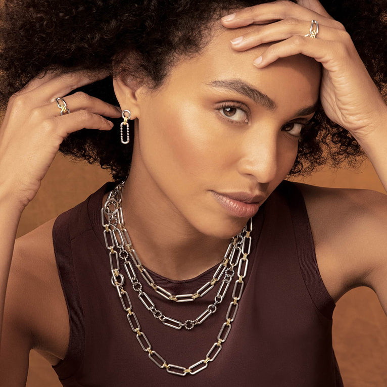 A woman is wearing a black tank top, necklace, and a pair of link drop earrings with Sterling silver and 18k gold variations of Caviar beading and fluting elements. 