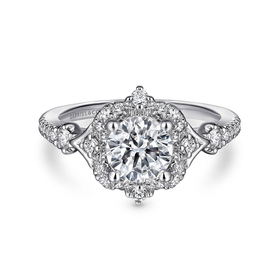 A white gold ring lies flat against a white background. It features a round-cut diamond set in the center with a petal-shaped diamond halo.