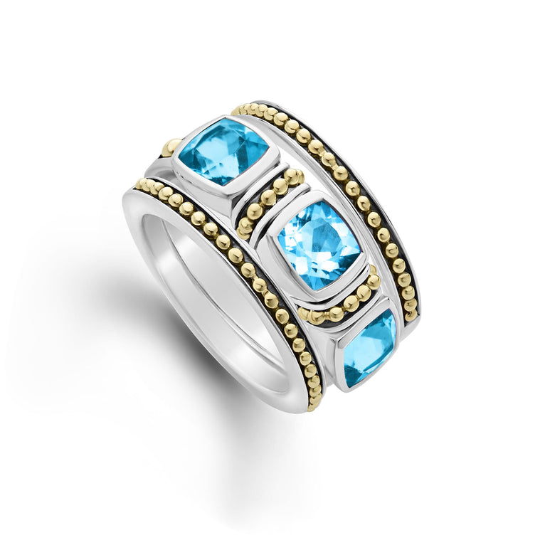 A sterling silver and 18k gold ring displayed angled in the middle of a white background featuring a trio of stacking rings with one swiss blue topaz ring and two 18K gold Caviar beaded rings with sterling silver accents.