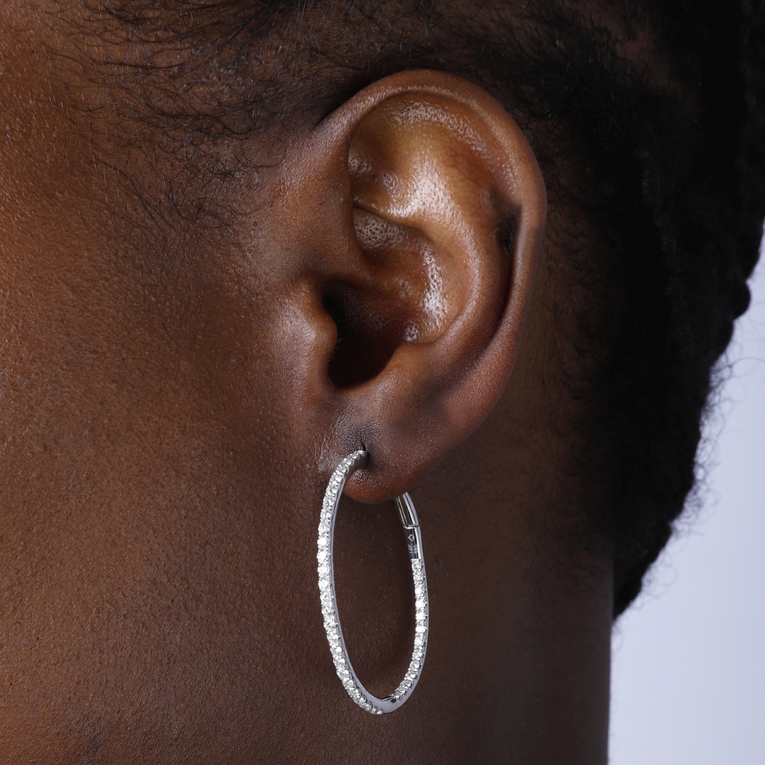 A woman with short black hair is wearing a pair of hoop earrings with a single row of round diamonds. 