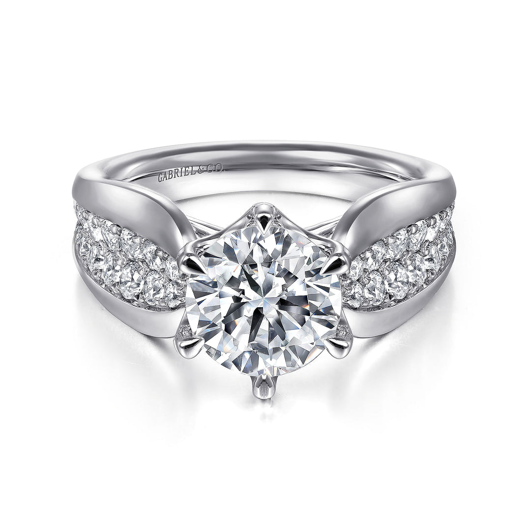 A white gold ring lies flat against a white background. It features a round-cut diamond set in the center with a sculptural shank