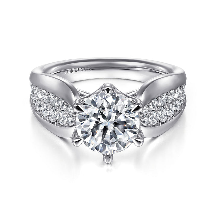 A white gold ring lies flat against a white background. It features a round-cut diamond set in the center with a sculptural shank