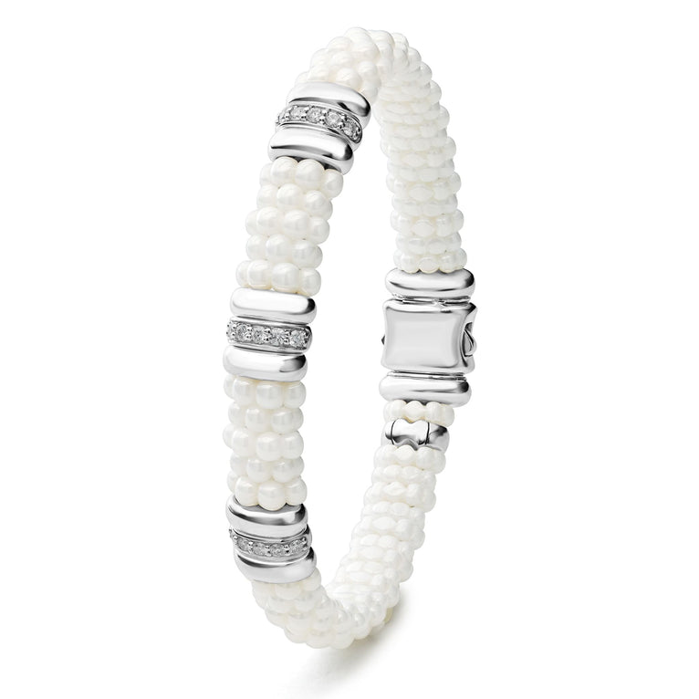 A sterling silver bracelet laid vertically in the middle of a white background featuring three diamond stations, white ceramic caviar beading, and sterling silver stations