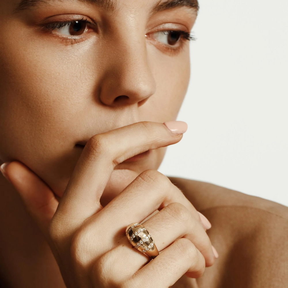 A close-up of a woman wearing a yellow-gold ring. The ring features five rows of round paved set diamonds on a domed-shaped signet ring with the "Michael M" inscription visible inside the band.