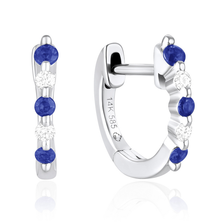 A pair of huggie earrings with alternating sapphire and white diamonds. The right earring is angled to the side.