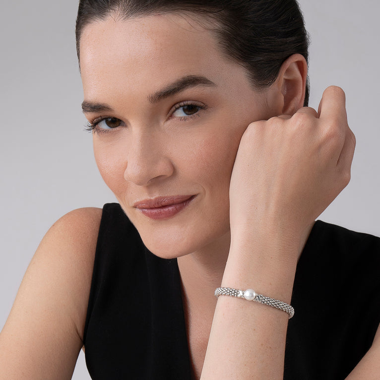 A woman is wearing a silver bracelet featuring freshwater cultured pearl framed by two sterling silver x stations.