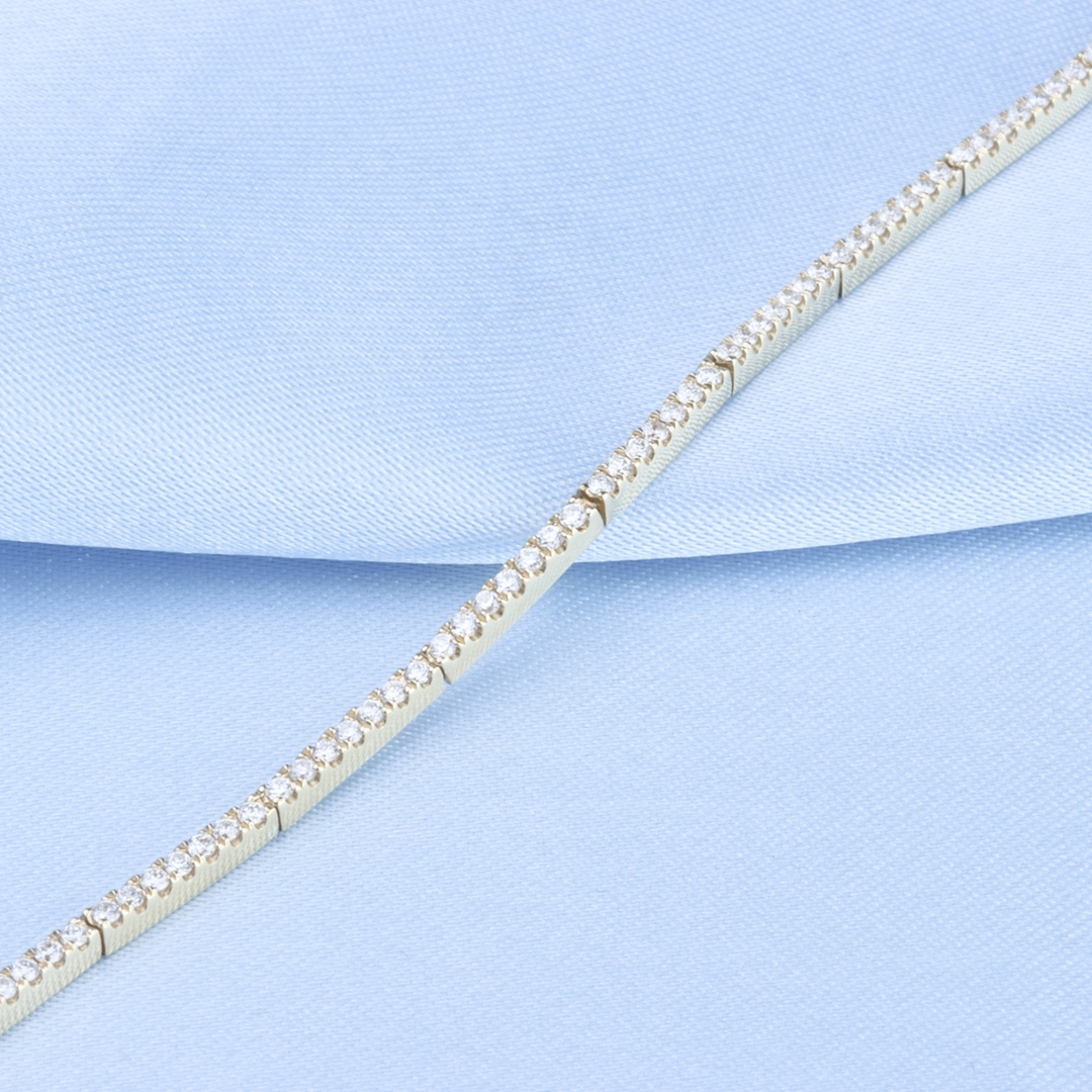 A yellow-gold bracelet laid out on a light blue background. It features sleek bars of pave-set diamonds.