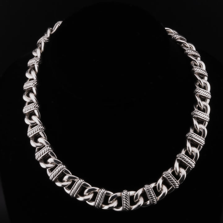 A sterling silver chain necklace with curb links and detailed stations against a black background.