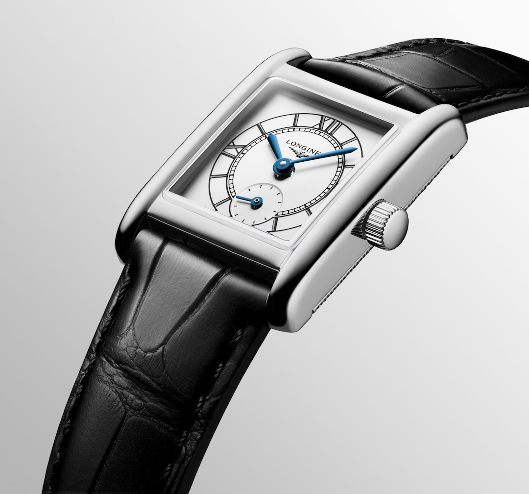 A Longines watch is displayed in the middle angled to the right on a white background. The rectangular-shaped watch features a white dial, blue hands, black markers, a stainless steel bezel, and a black leather strap.