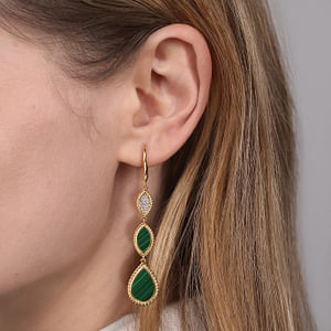 A woman with blonde hair is wearing a pair of drop earrings with a rope design including a diamond and malachite gemstones.