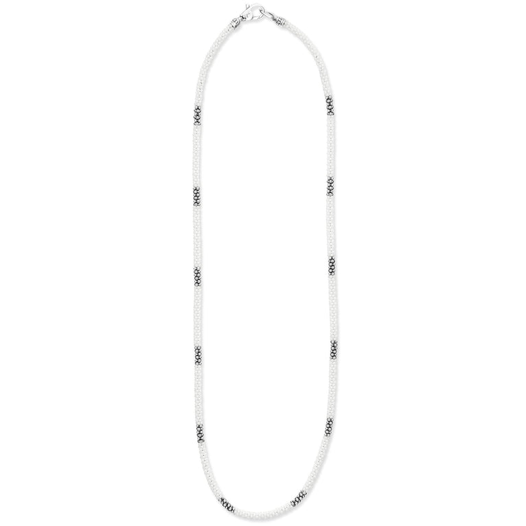 A sterling silver and ceramic beaded necklace in the middle of a white background featuring white ceramic and silver Caviar beading.