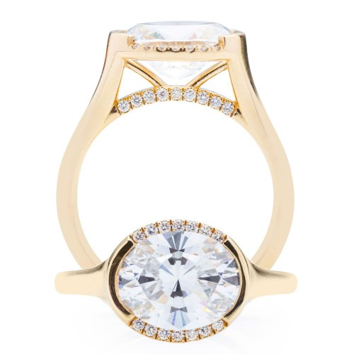 A side-view of the Oval East-West Semi Halo Engagement Ring, made of yellow gold. The side view shows the diamond's pavilion and the yellow-gold band. It also shows the ring lying flat below the side view ring.