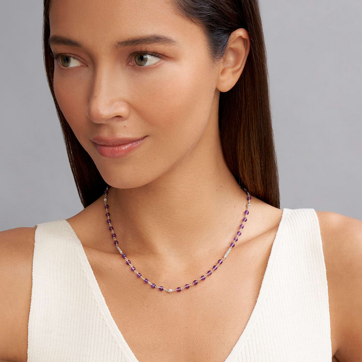 A woman is wearing a sterling silver and ceramic beaded necklace featuring Amethyst ceramic and silver caviar beading.