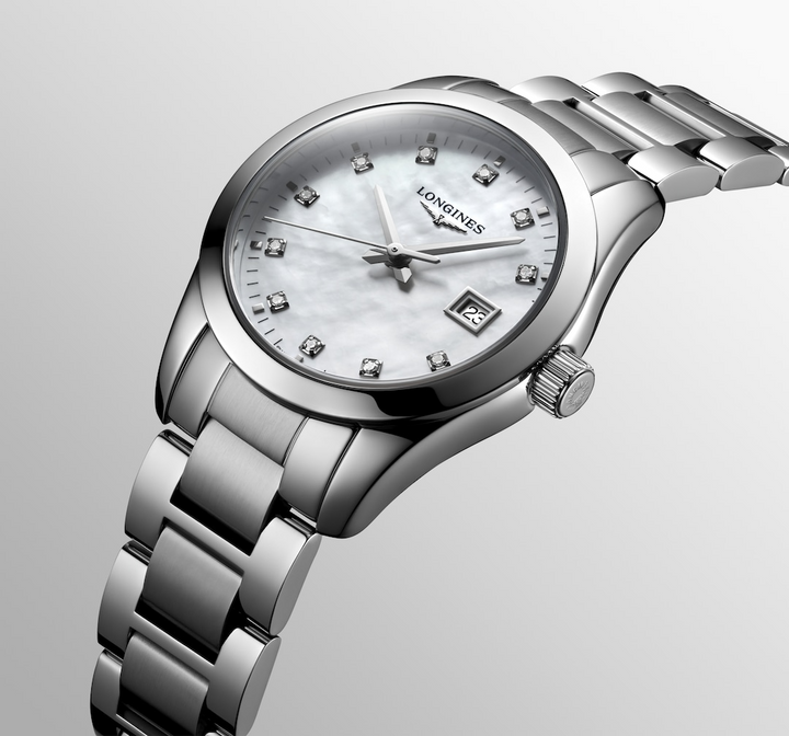 A Longines watch is displayed in the middle angled to the right on a white background. The watch features a white mother-of-pearl diamond-set dial, silver hands and markers, a stainless steel bezel, and a stainless steel bracelet.