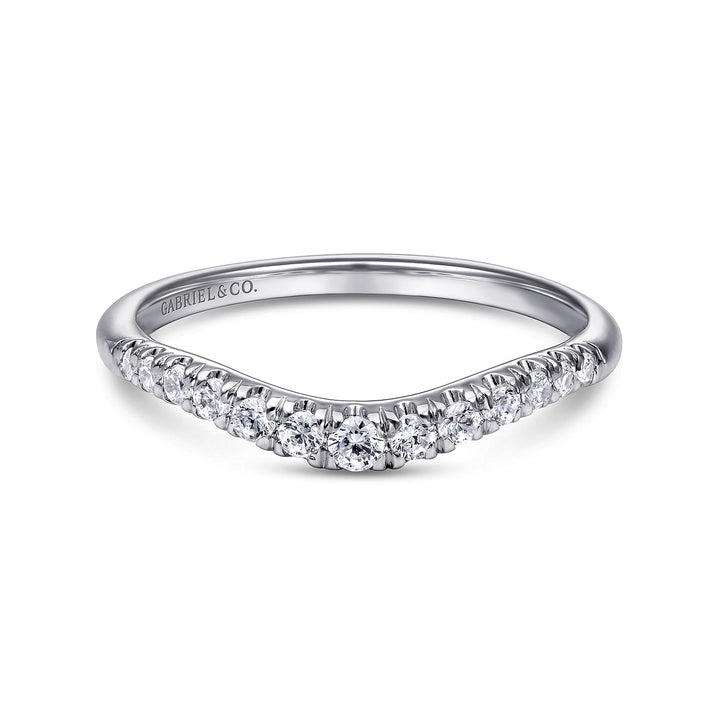 A white gold ring lies flat against a white background. The curved band features round diamonds with a shared prong. 