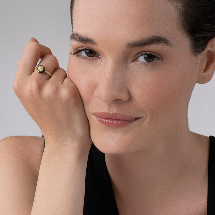 A woman wearing An 18K Gold ring in the middle of a white background featuring caviar beading framed by black ceramic