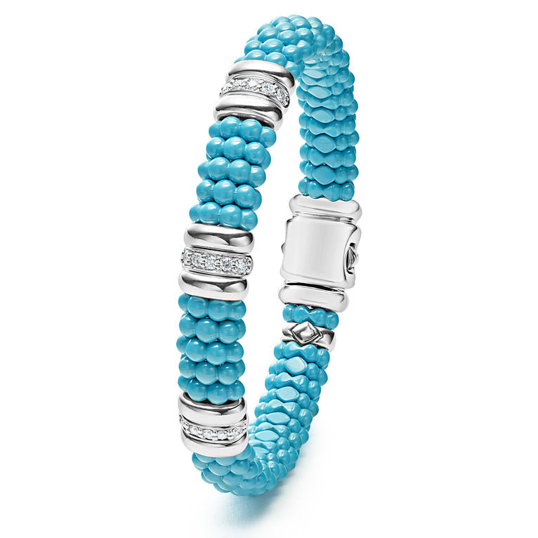 A sterling silver bracelet laid vertically in the middle of a white background featuring three diamond stations, blue ceramic caviar beading, and sterling silver stations