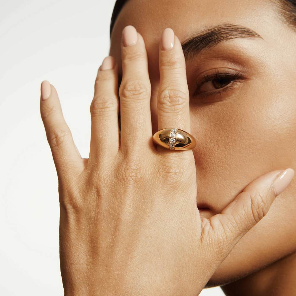 A close-up of a woman wearing a yellow gold ring with a unique band with a diamond set row in the middle.