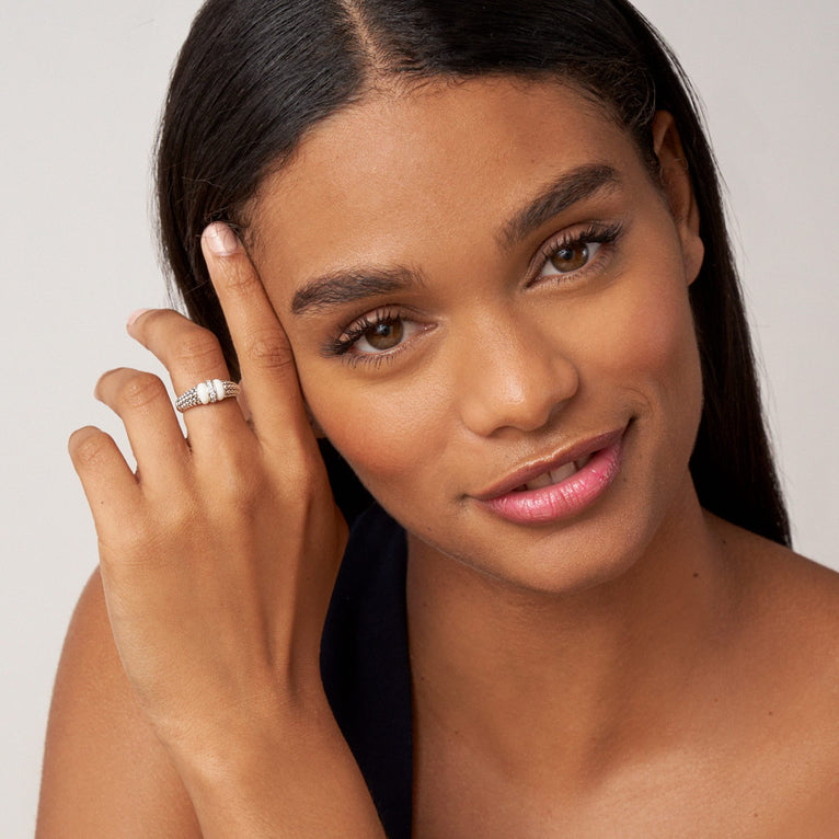 A woman is wearing a sterling silver ring featuring white ceramic caviar beading with a row of diamonds.