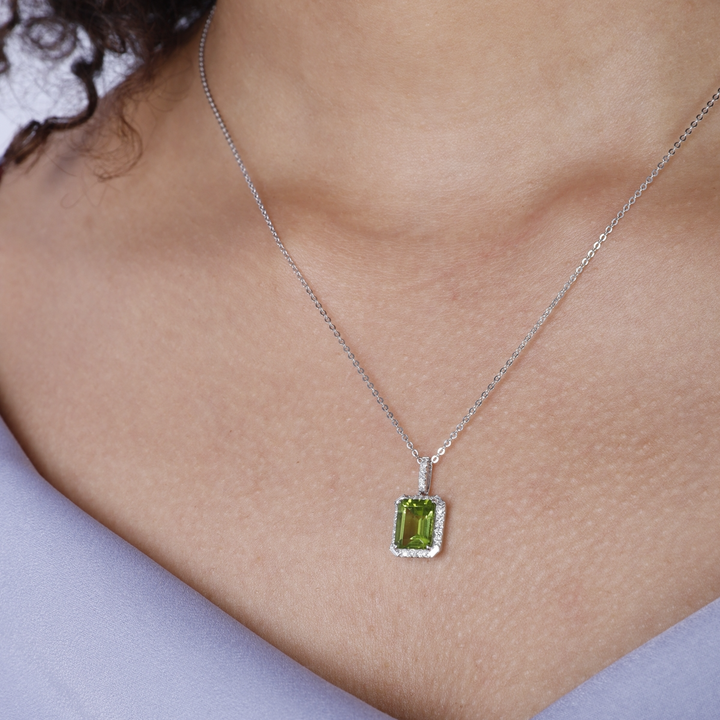 A woman is wearing a white-gold Emerald Cut Necklace and purple top. The necklace features a cushion-cut light green center stone and an 18k white gold chain.