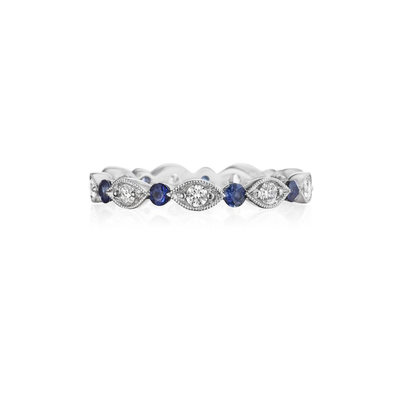 A white gold ring lies flat against a white background. It features a diamond set band with marquise and sapphire detailing.