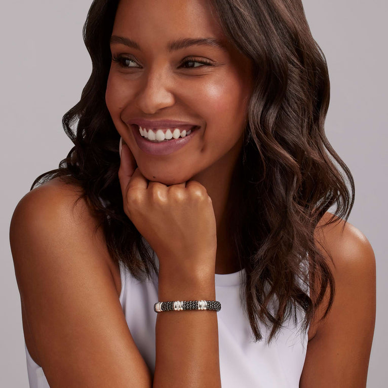 A woman wearing a sterling silver bracelet, featuring three diamond stations, black ceramic caviar beading, and sterling silver stations