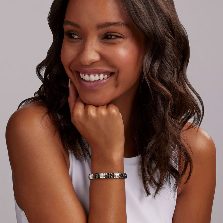 A woman wearing a sterling silver bracelet, featuring three diamond stations, black ceramic caviar beading, and sterling silver stations