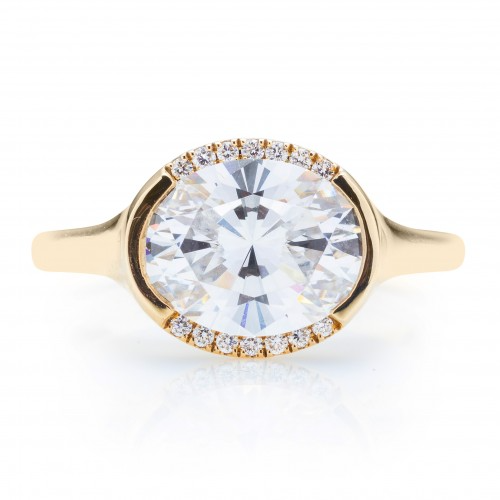 The Oval East West Semi Halo Engagement Ring, made of yellow gold, lies flat against a white background. It features an oval-cut diamond set in the center with a semi-halo of diamonds