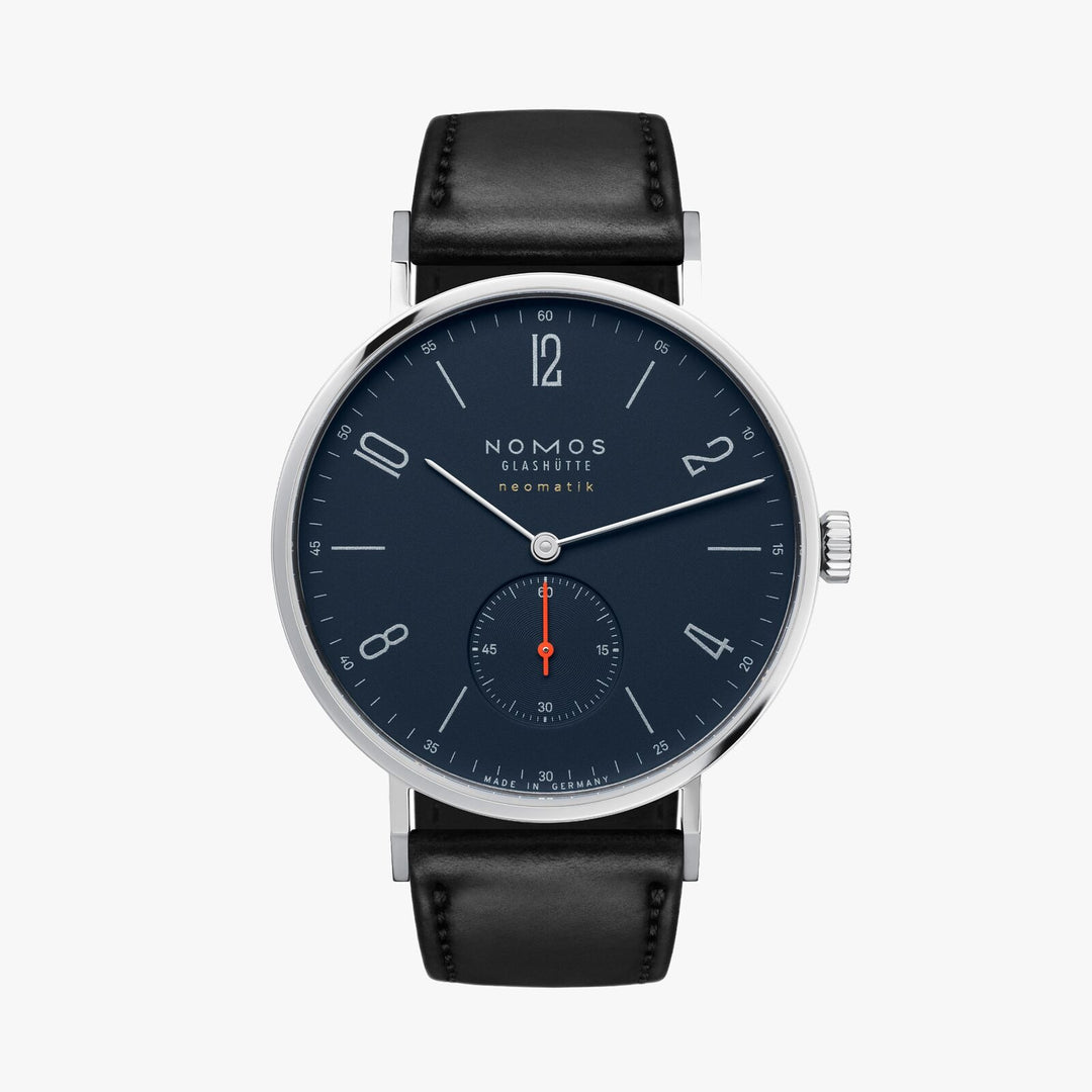 A Nomos Glashutte watch stands straight against a white background. It features a dark blue dial, white hands and markers, a stainless steel bezel, and a black strap.