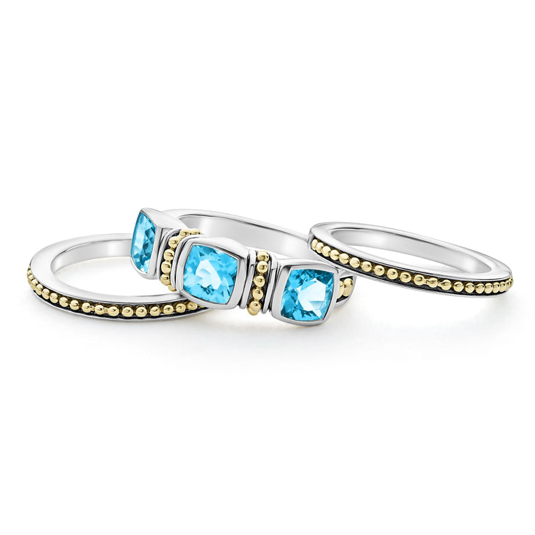 A side-view of a sterling silver and 18k gold ring displayed in the middle of a white background featuring a trio of stacking rings with one swiss blue topaz ring and two 18K gold Caviar beaded rings with sterling silver accents.