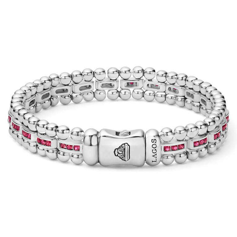 A sterling silver link bracelet in the middle of a white background highlights the clasp and features ruby gemstones and caviar bead links.