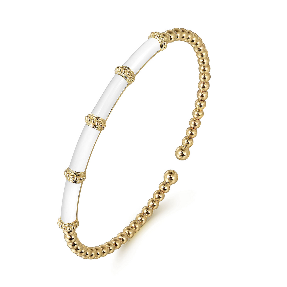 A yellow-gold bangle bracelet with a beaded band, white enamel stations, and end caps is angled in the middle of a white background.