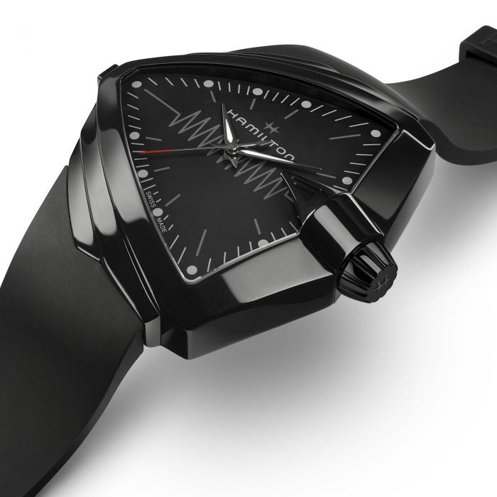 A Hamilton triangular-shaped watch is laid out and tilted to the right against a white background. It features a black dial, white hands and markers, a steel PVD black coating case, a black bezel, a steel crown, and a black rubber strap.