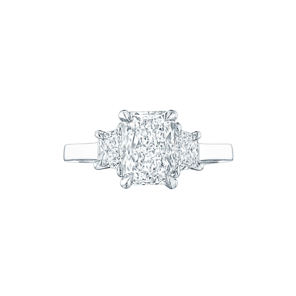 The Radiant and trapezoid Diamond Ring, made of white gold, lies flat against a white background. It features a radiant-cut diamond set in the center with side diamonds.