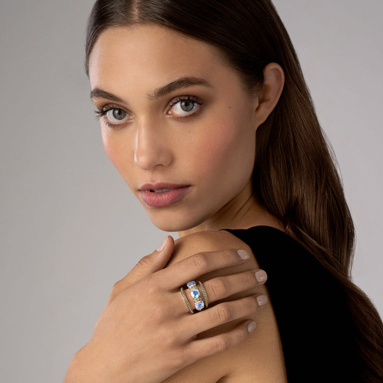 A woman is wearing a sterling silver and 18k gold ring featuring a trio of stacking rings with one swiss blue topaz ring and two 18K gold Caviar beaded rings with sterling silver accents.