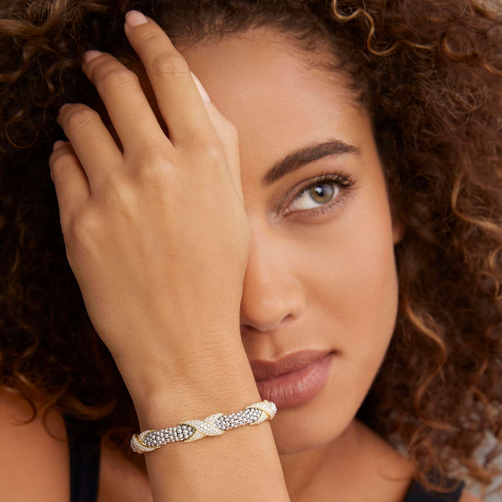 A close-up of a woman wearing a black top and a Sterling Silver & 18k gold bracelet. The bracelet features diamond-set X stations, caviar beading, and a stainless steel clasp.